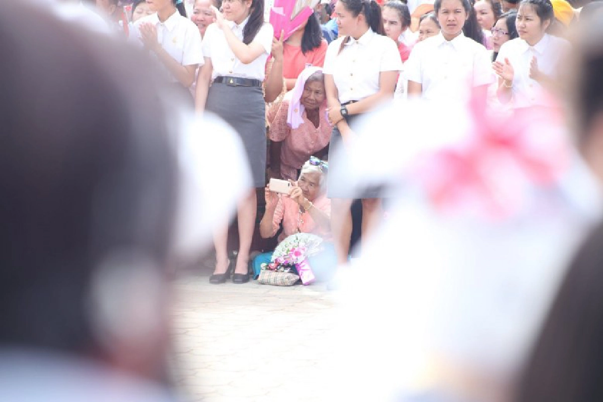 ยายนั่งลงกับพื้น รอถ่ายรูปหลานที่กำลังเดินมาในขบวนบัณฑิต