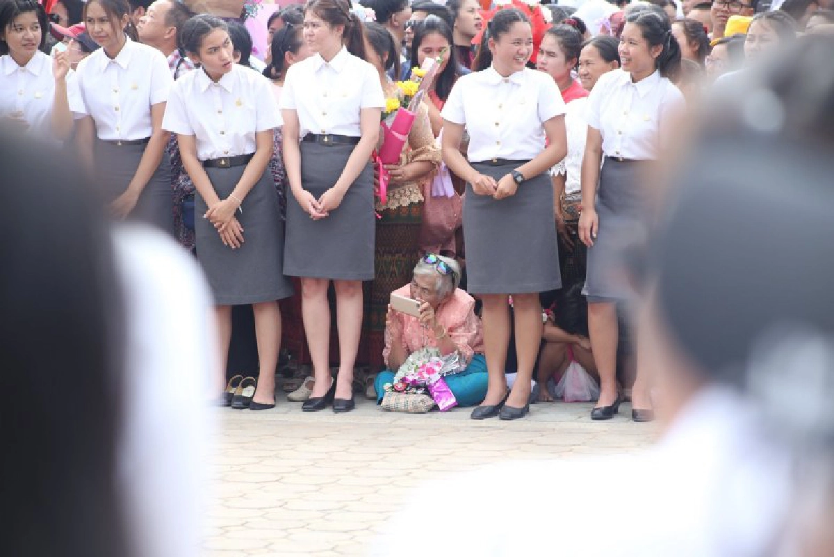 ยายนั่งลงกับพื้น รอถ่ายรูปหลานที่กำลังเดินมาในขบวนบัณฑิต