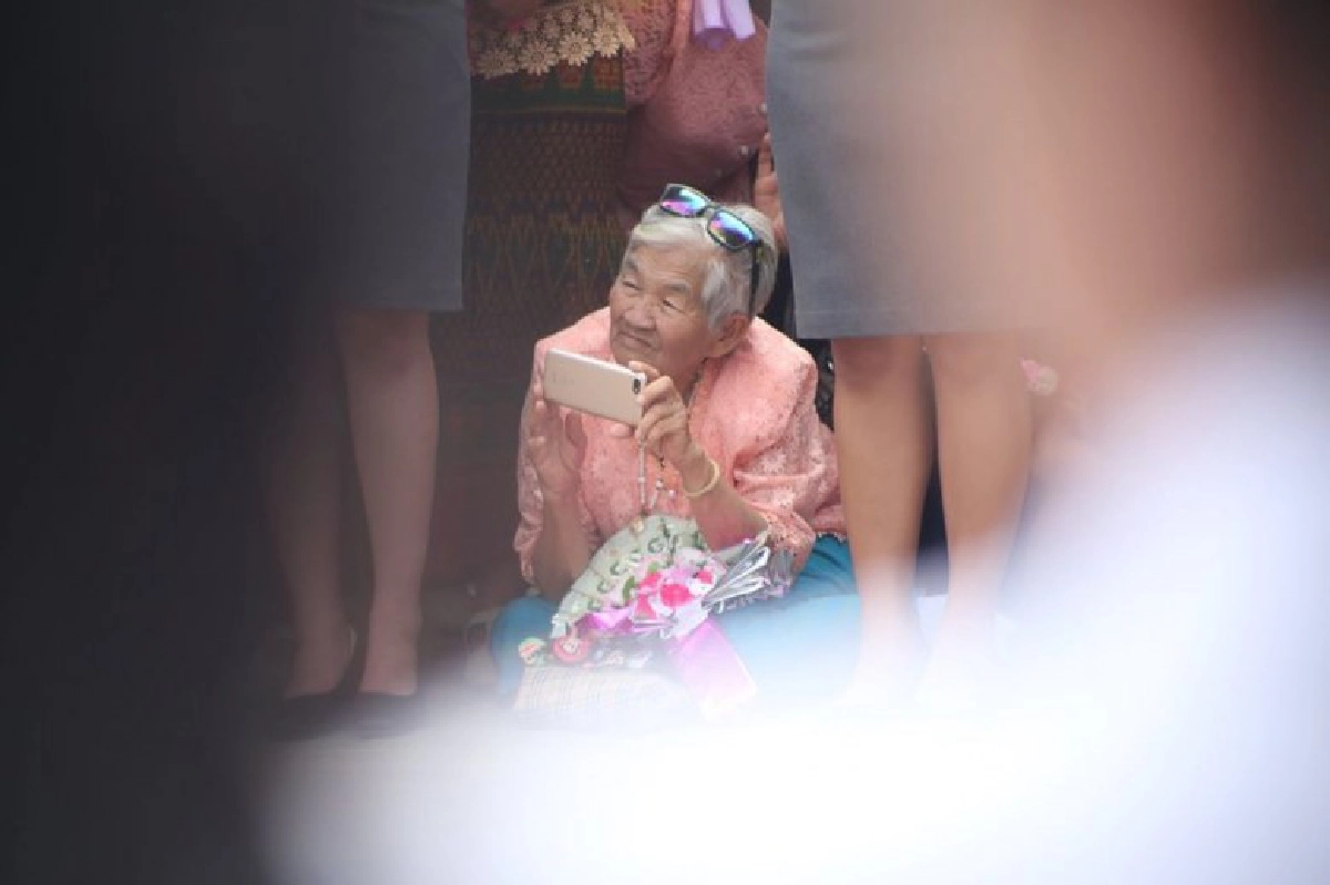 ยายนั่งลงกับพื้น รอถ่ายรูปหลานที่กำลังเดินมาในขบวนบัณฑิต