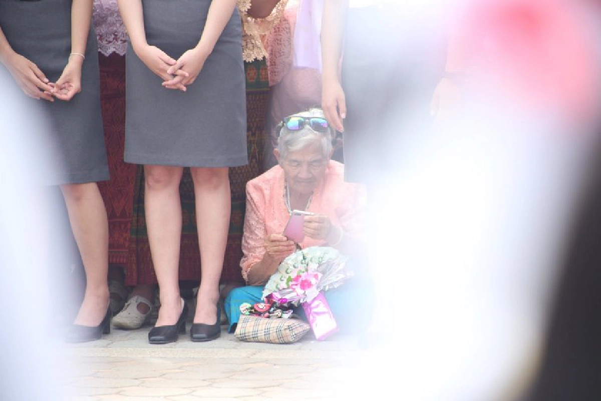 ยายนั่งลงกับพื้น รอถ่ายรูปหลานที่กำลังเดินมาในขบวนบัณฑิต